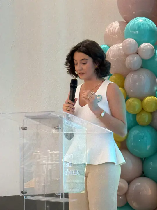 Conductora con blusa blanca habla desde el podio de acrílico.