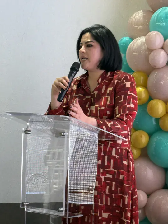 Ponente con vestido estampado rojo habla con micrófono desde el podio.