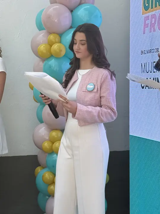 Participante con saco rosa lee su intervención frente a la pantalla del foro Mujeres Transformando.