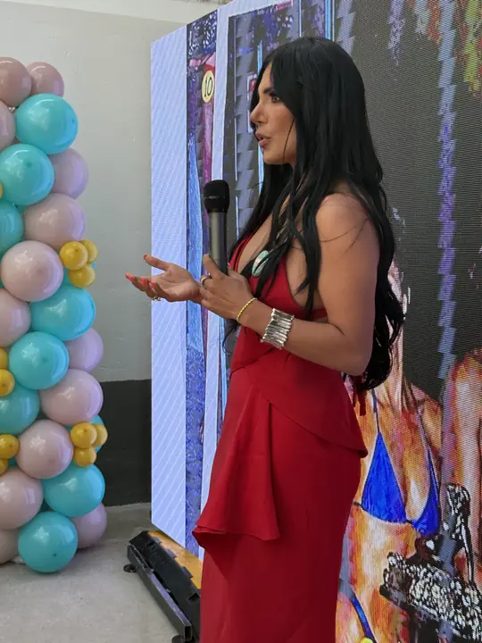 Ponente con vestido rojo se dirige al público junto a la columna de globos turquesa, rosa y amarillo.