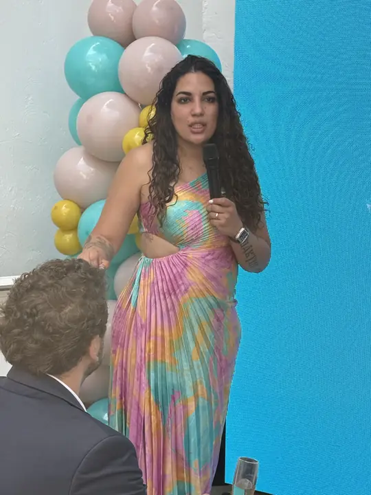 Participante de cabello rizado habla con micrófono junto a los globos de la marca.