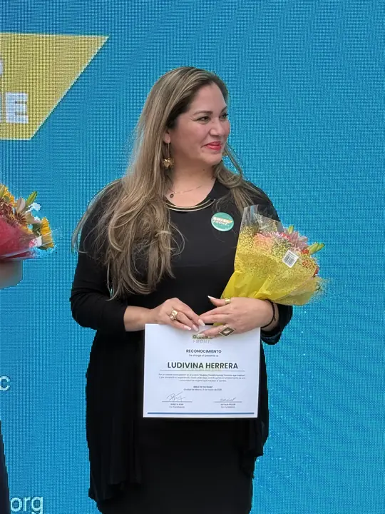 Participante sostiene su reconocimiento y un ramo de flores.