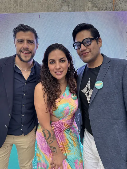 Tres asistentes posan juntos frente a la pantalla del evento.