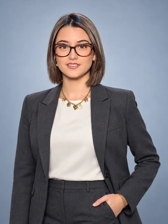 Retrato de Natalia Paulín con lentes y traje gris sobre fondo azul.
